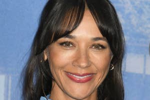 Rashida Jones smiling, wearing a high-neck, satin-textured blue dress. She has long, wavy hair with bangs