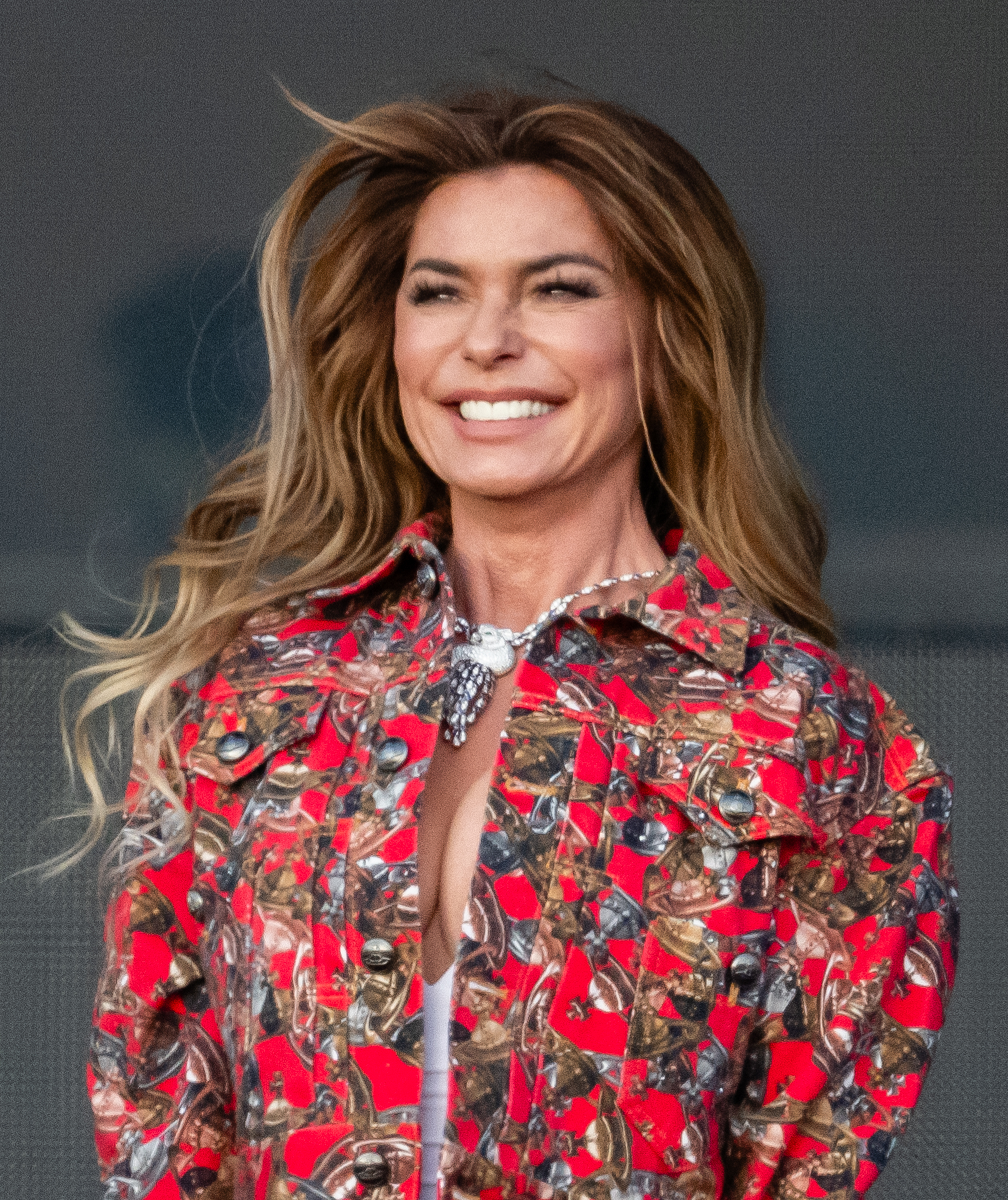 Shania Twain smiling, wearing a patterned jacket with a statement necklace