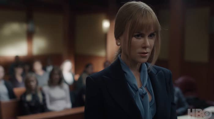 Nicole Kidman, in a courtroom scene from Big Little Lie, wearing a tailored suit with a blue scarf tied at the neck