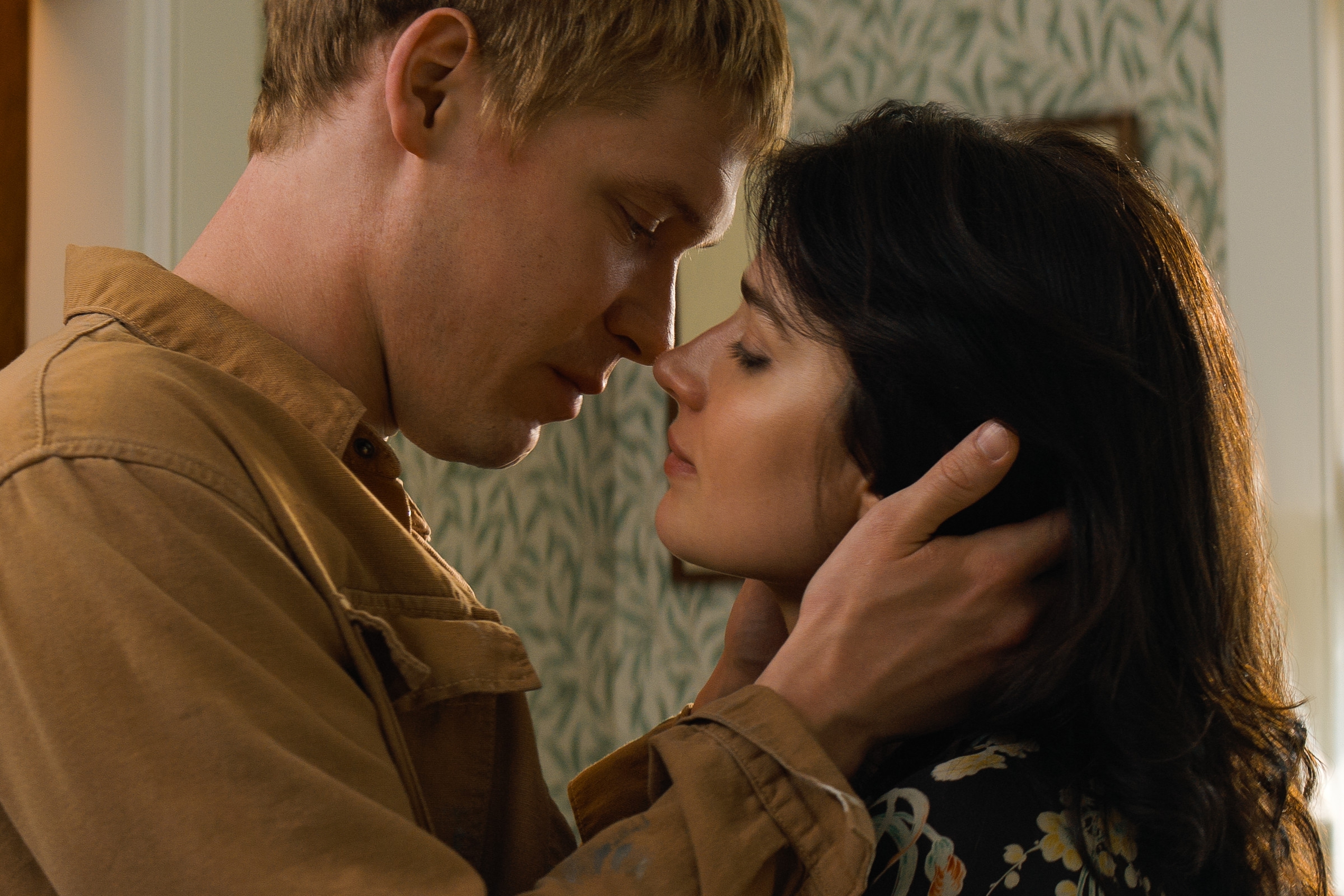 A close-up of Billy Howle and Eve Hewson about to kiss in a tender moment. Joe wears a casual jacket, while Letitia wears a floral-patterned outfit