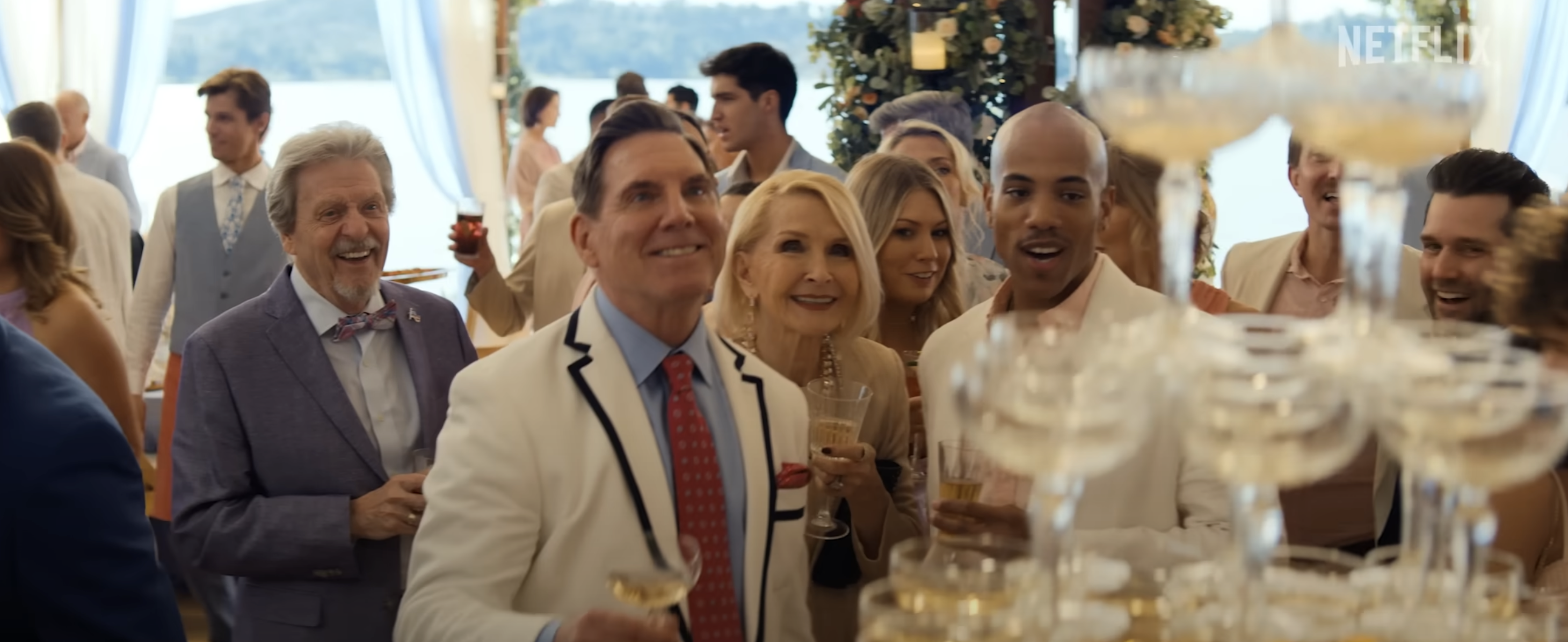 A group of elegantly dressed people, including Al Pacino, Josh Brolin, and Toni Collette, smiling and toasting with champagne at a sophisticated gathering