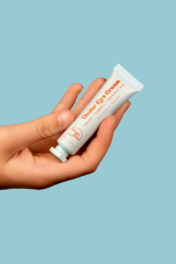 A hand holding a tube of under-eye cream with visible text on the tube reading &quot;Under Eye Cream.&quot;