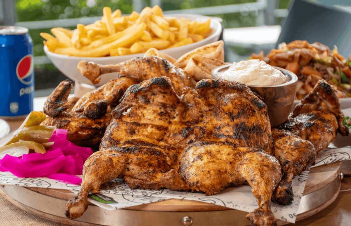 Grilled spatchcock chicken served with fries, pickled vegetables, and a bowl of dipping sauce. A can of Pepsi is on the side