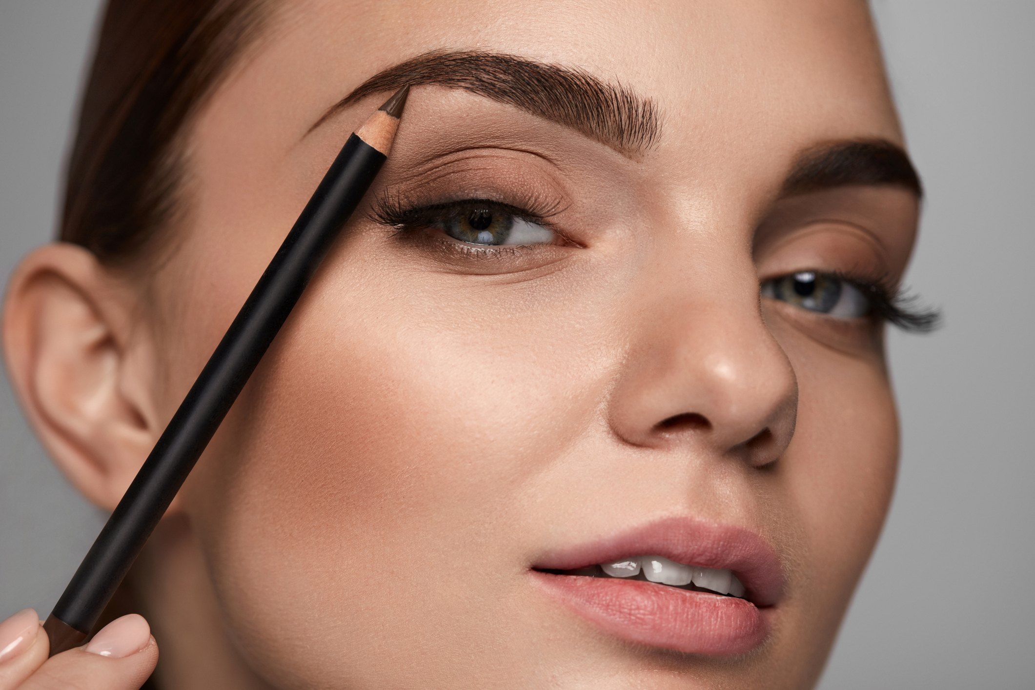 Close-up of a woman using an eyebrow pencil to fill in her eyebrow, showcasing a makeup routine