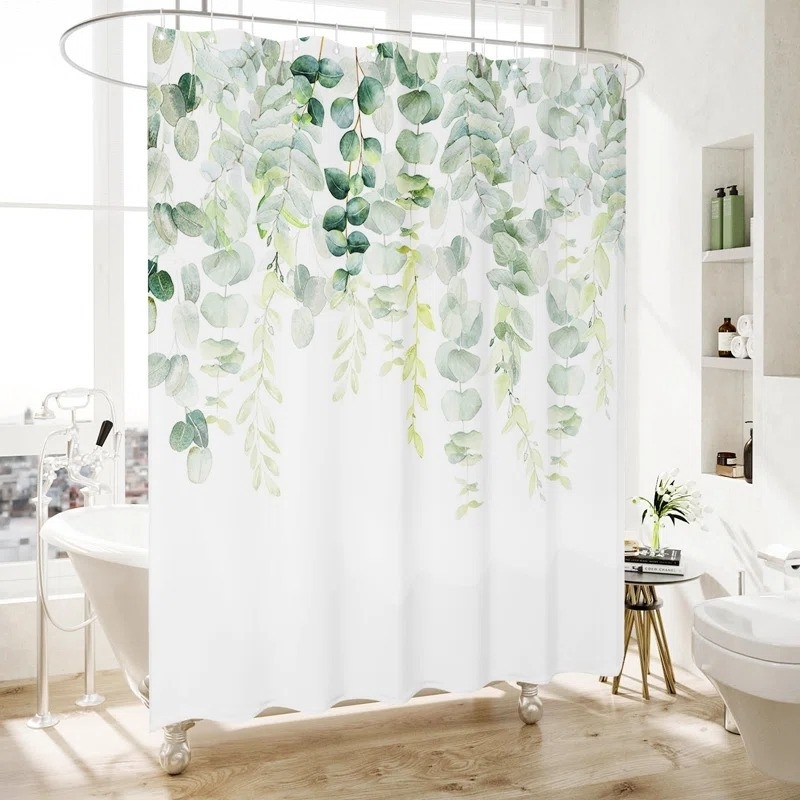 Shower curtain with a botanical print of hanging green leaves in a modern, minimalistic bathroom with wooden floor and white fixtures