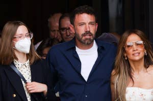 Ben Affleck, Jennifer Lopez in a floral dress, and a masked woman in a polka dot dress and blazer walking together with people in the background