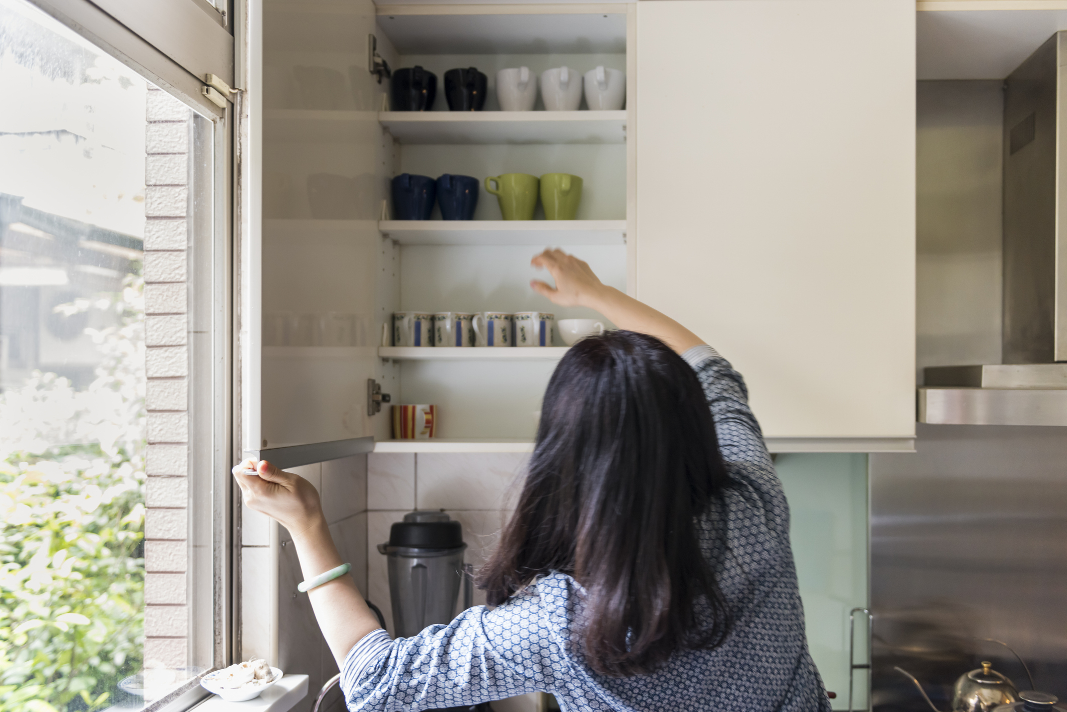 Person reaching for mugs in a kitchen cabinet