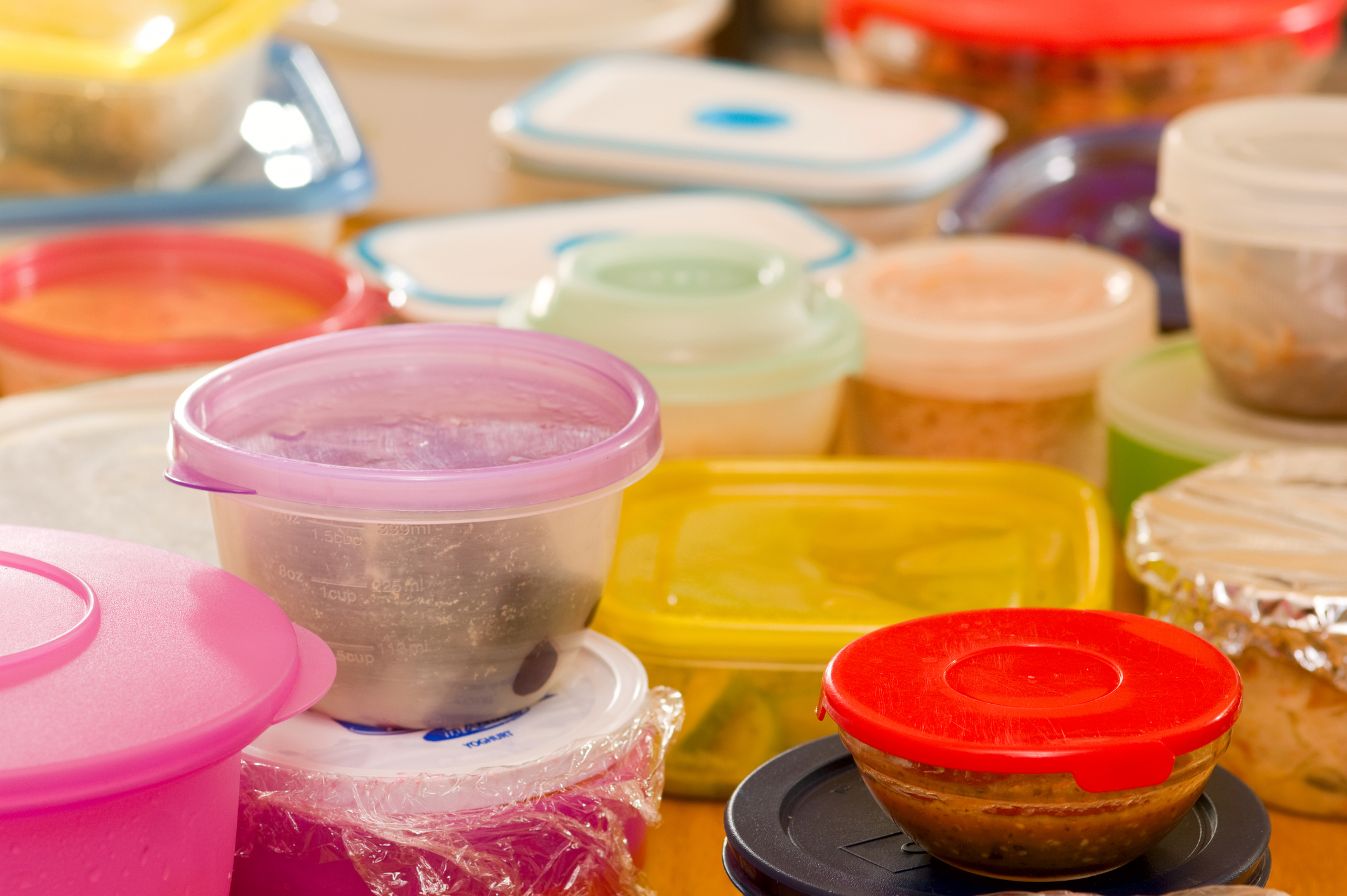 Various food storage containers, some with lids and others covered with plastic wrap, are arranged together in this kitchen scene