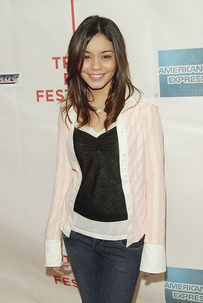 Vanessa Hudgens at a film festival, wearing a casual outfit: light jacket over a black top paired with jeans. She is smiling and posing in front of a banner