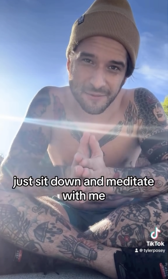 Tyler Posey, sitting outdoors without a shirt and showing extensive tattoos, invites viewers to sit down and meditate with him