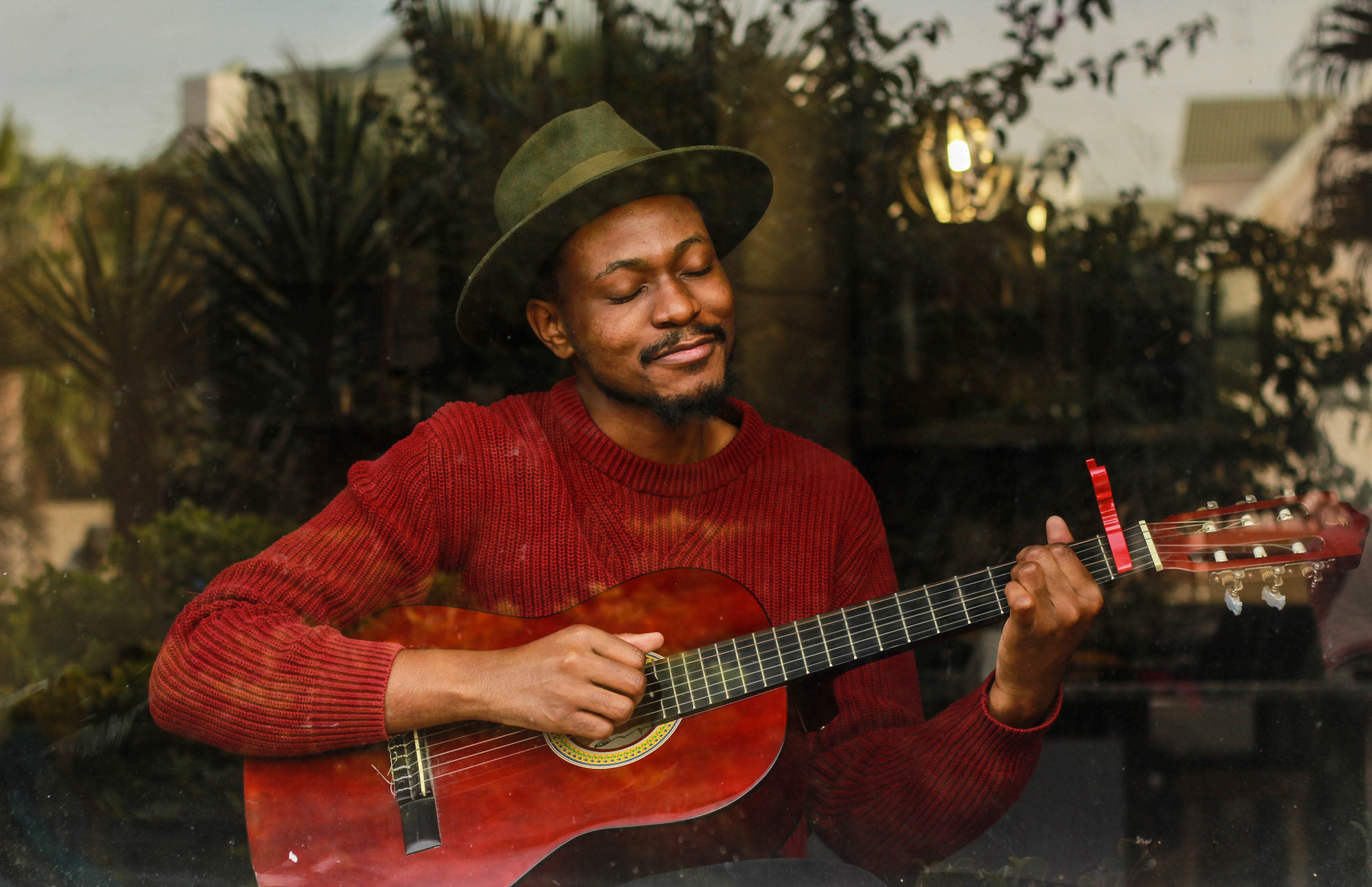Man in a red sweater and green hat playing an acoustic guitar with a content expression on his face
