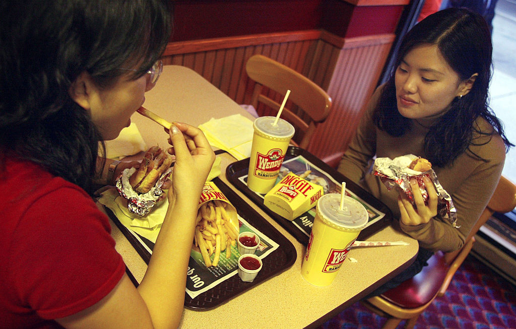 Two people are eating at a Wendy&#x27;s fast food restaurant, with trays of fries, drinks, and burgers in front of them