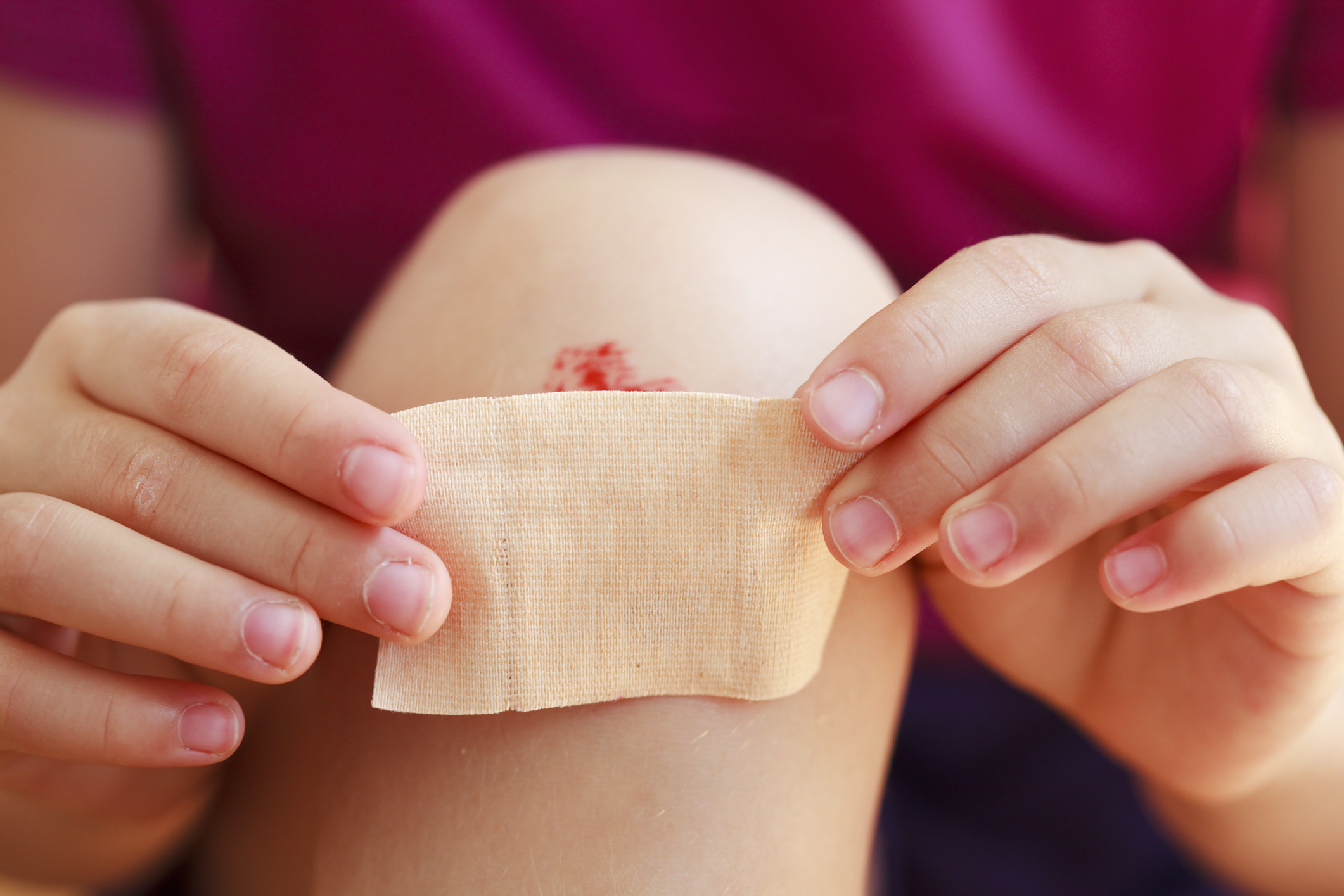 A person placing a band-aid over a scraped knee, focusing on the hands and the injured knee