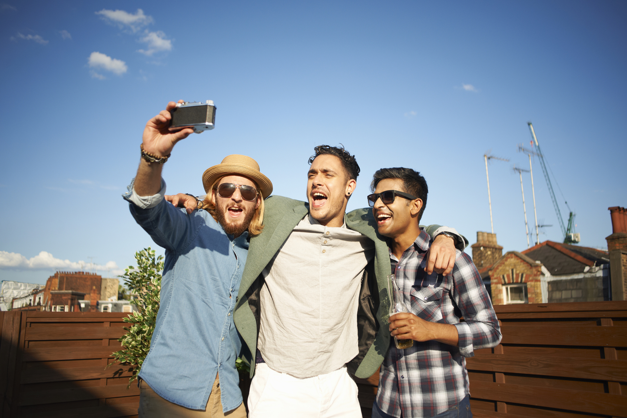 Three men take a joyful selfie outdoors on an urban patio with one holding a camera