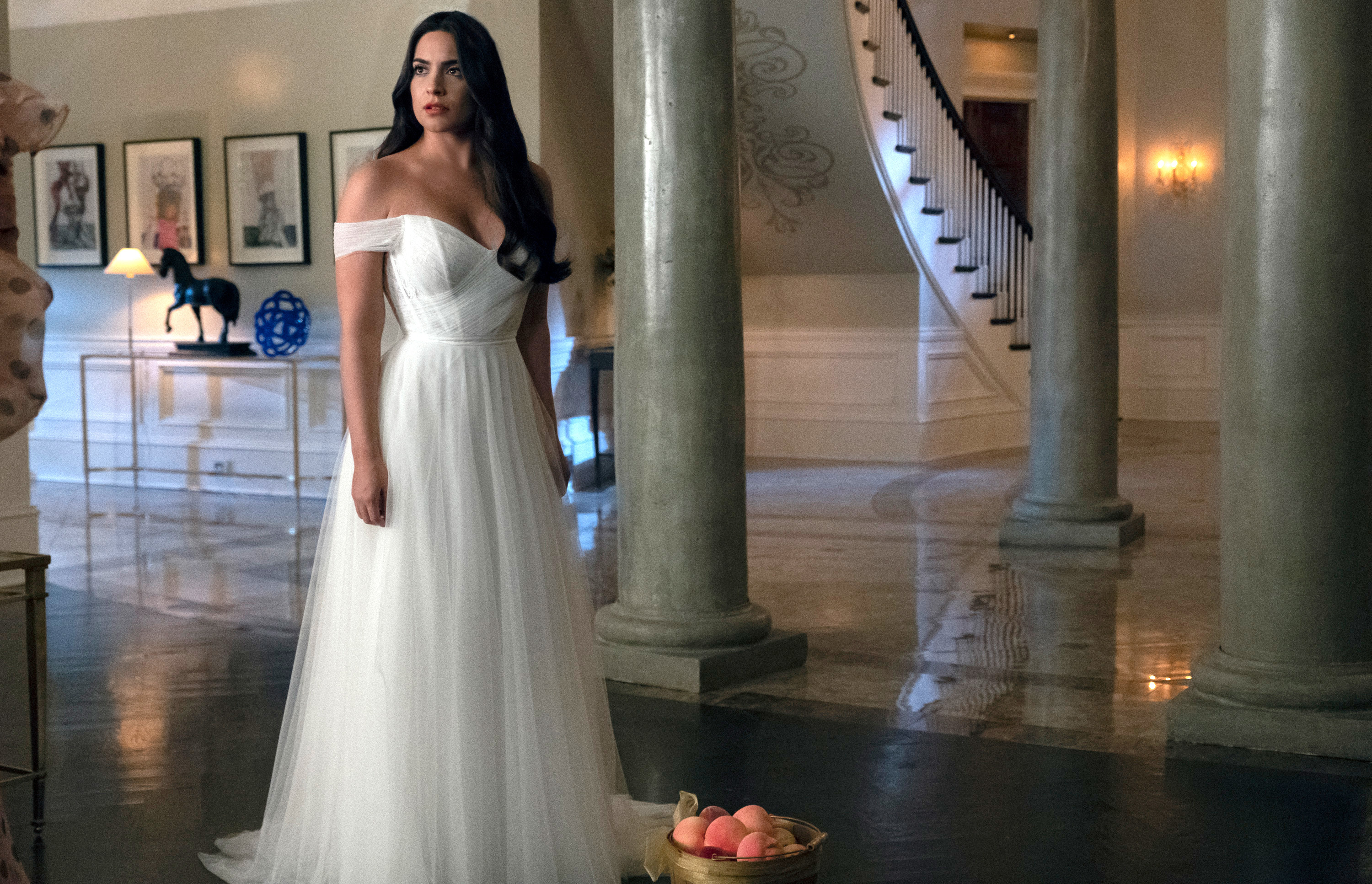 Cristal stands in an elegant off-shoulder bridal gown in a stately, ornate room with columns