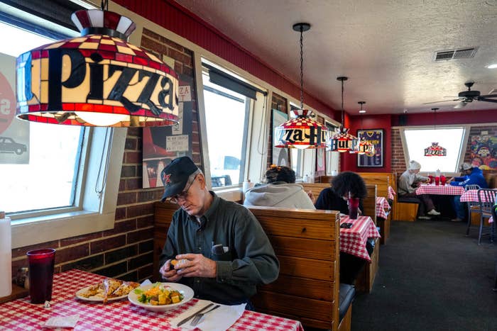 Customers dining under pizza-themed lights in a cozy restaurant with checkered tablecloths and wood-paneled booths