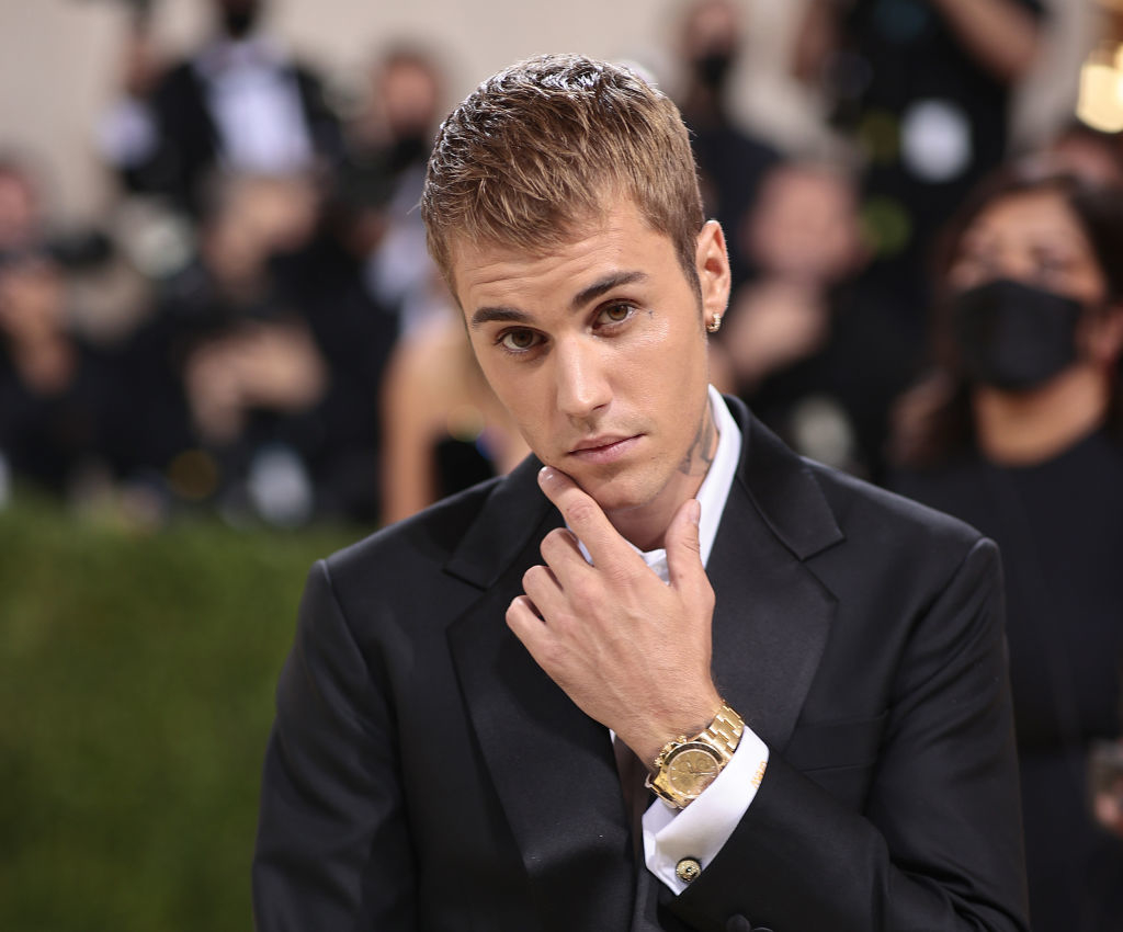 Justin Bieber on the red carpet, wearing a black suit and gold wristwatch, posing with his hand on his chin