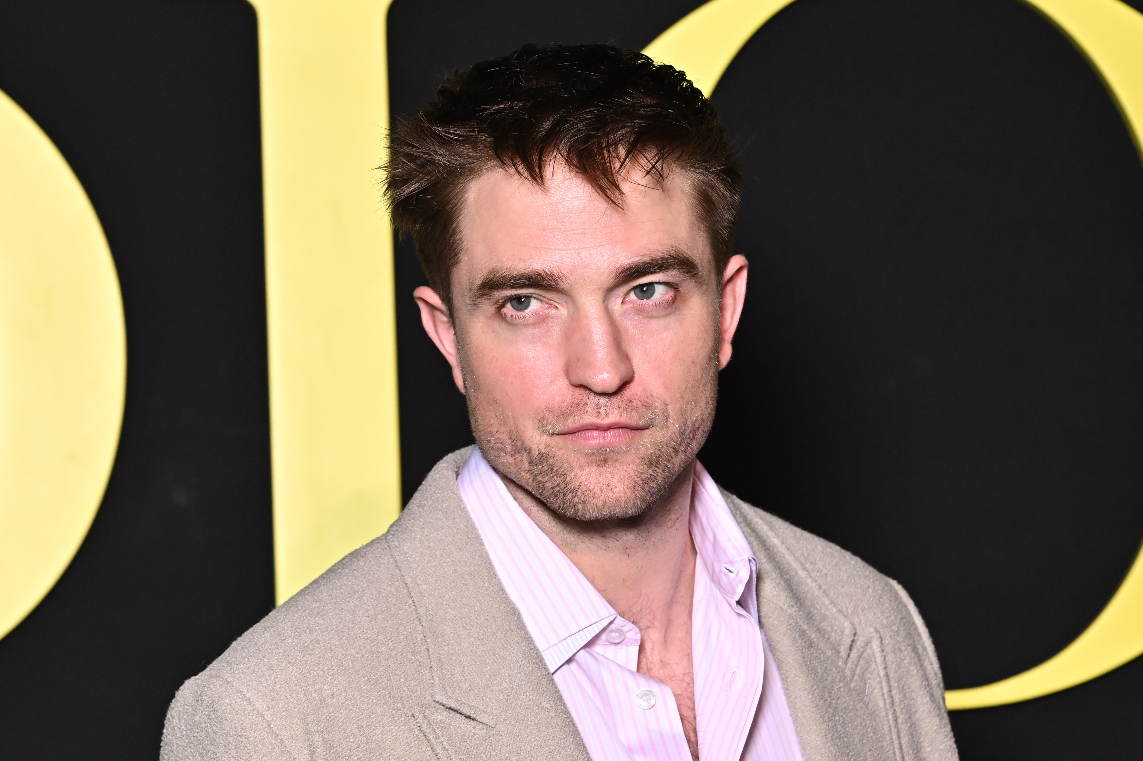 Robert Pattinson wears a light blazer and a collared shirt at an event