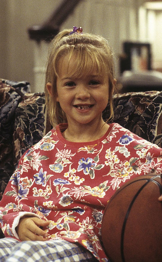 Young Morgan sitting on a couch with a basketball, wearing a floral sweater and checkered pants, smiling at the camera