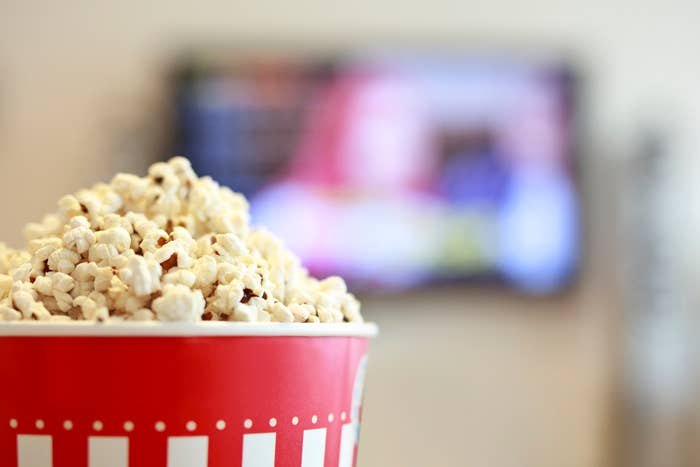 A close-up of a bucket of popcorn in a red and white container, with a blurred television screen in the background