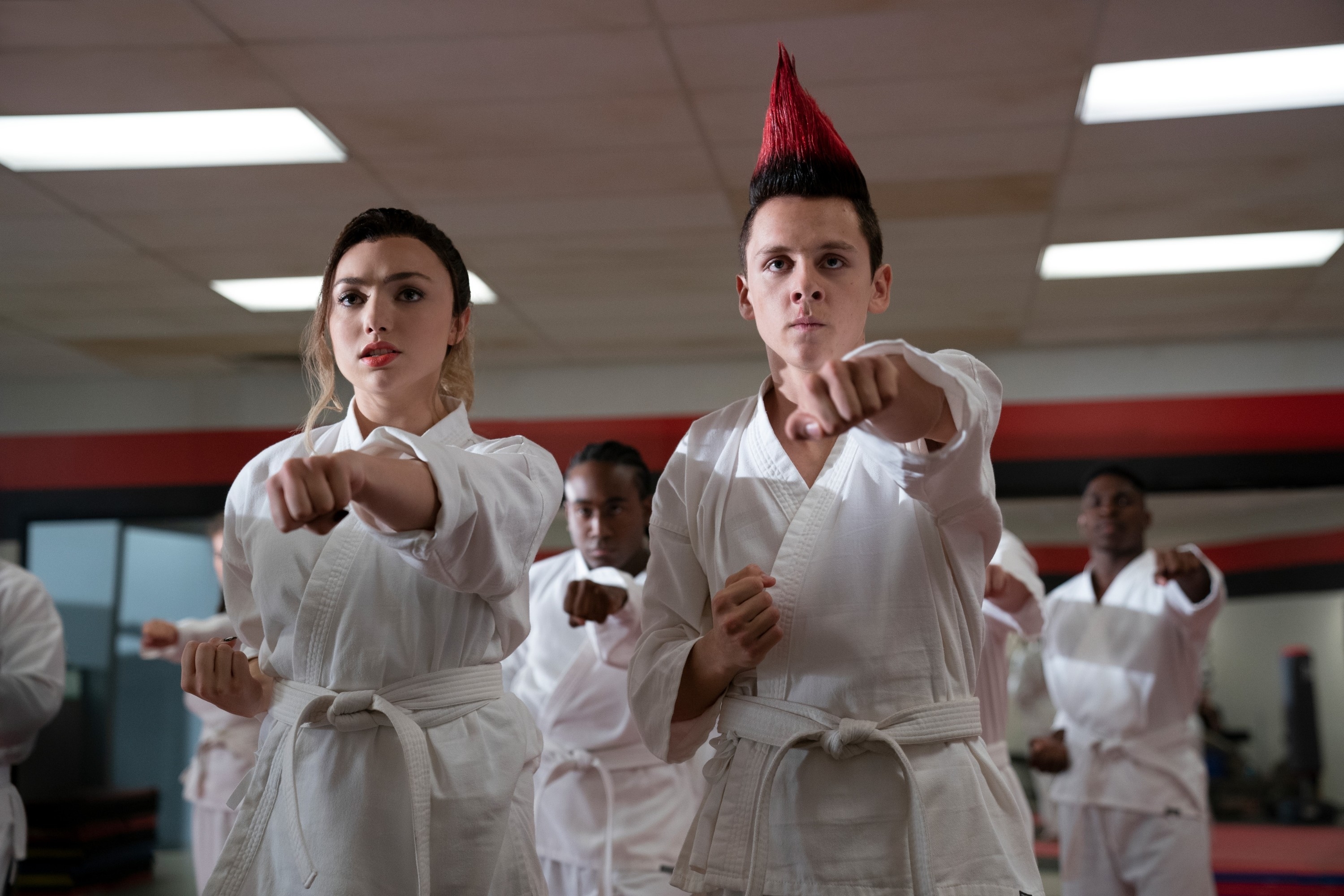 Peyton List and Jacob Bertrand in martial arts uniforms performing a punch in a martial arts class in &quot;Cobra Kai&quot;