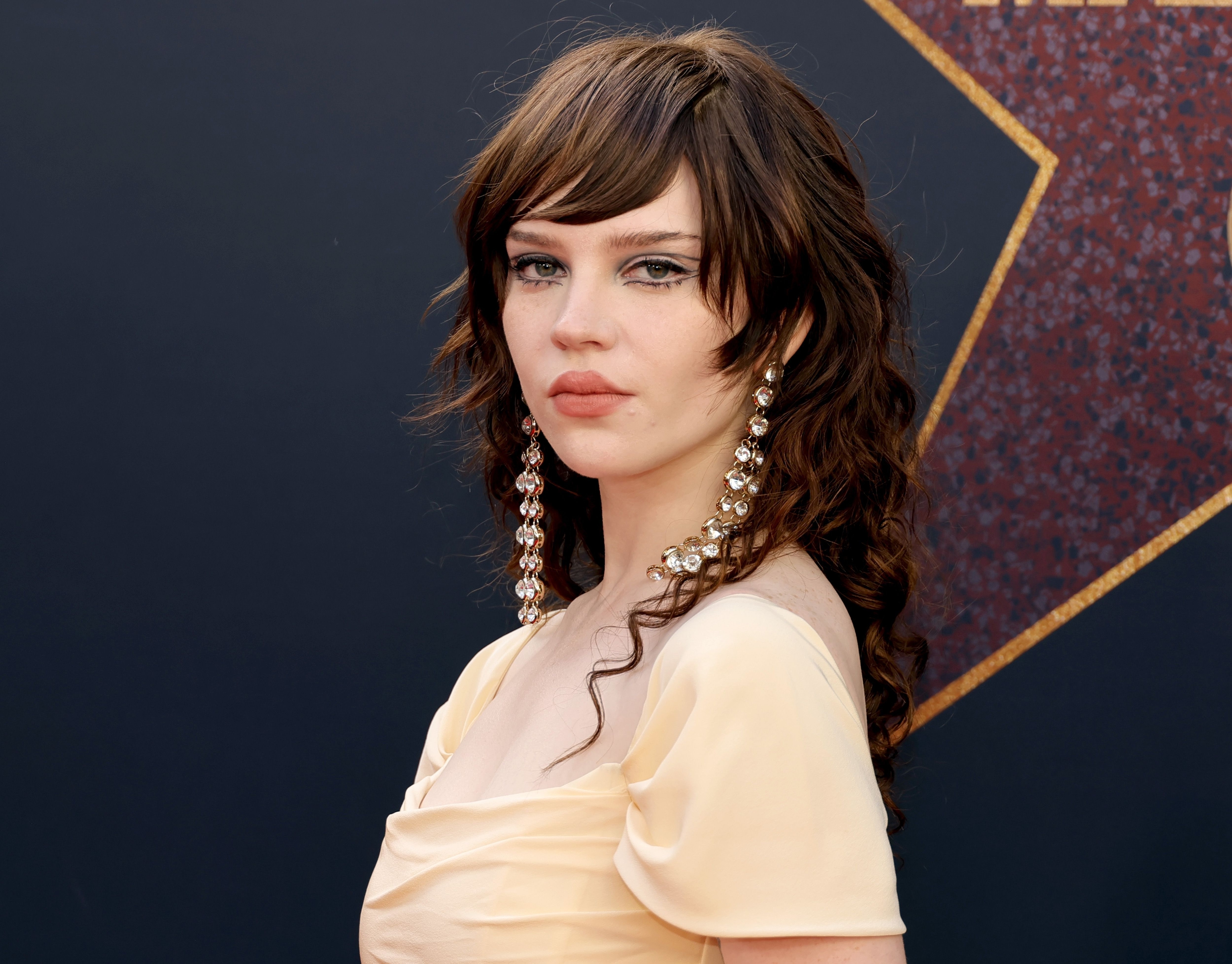 Sophie Thatcher wearing a yellow outfit and long earrings at the premiere of &quot;MaXXXine&quot;