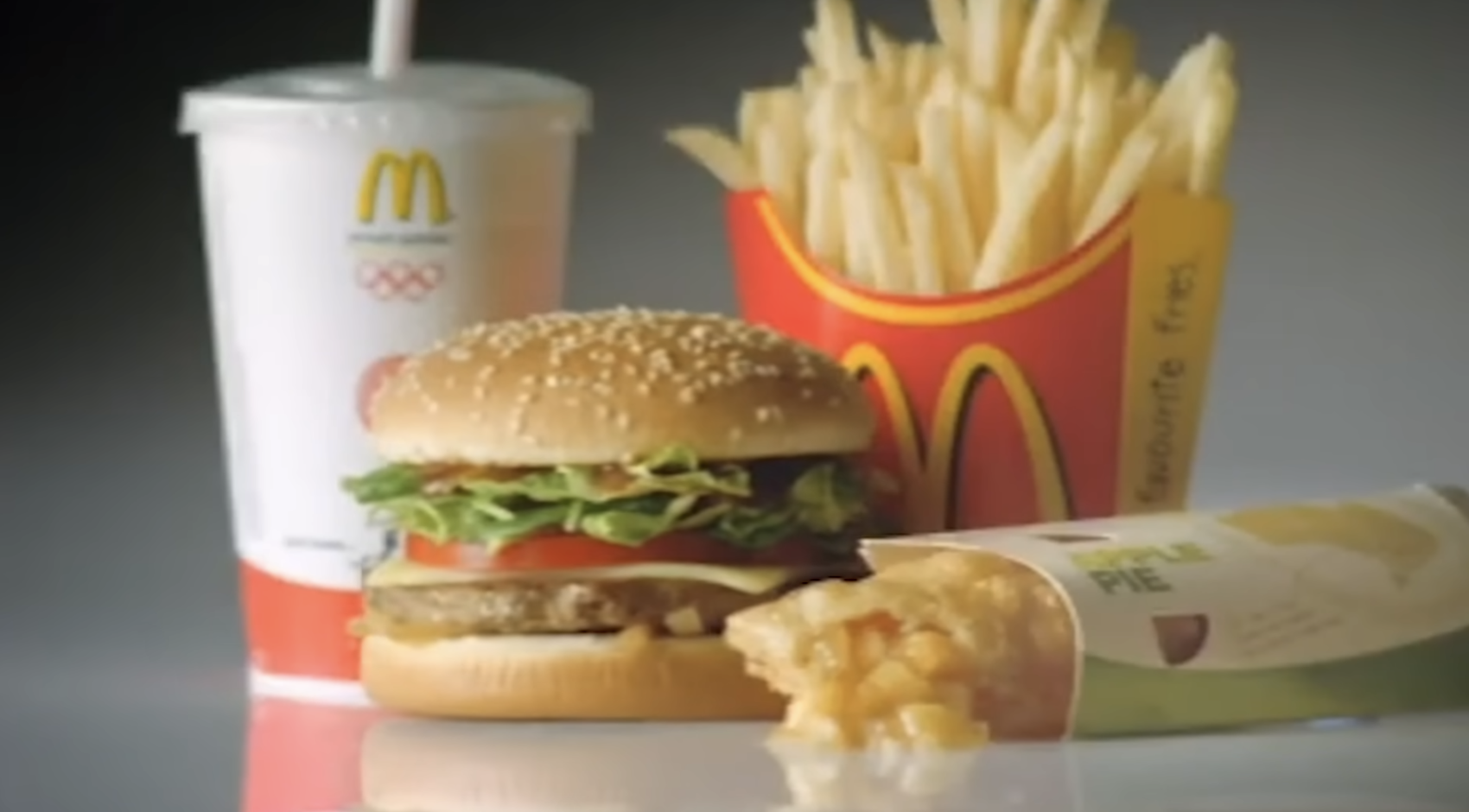 McDonald&#x27;s meal featuring a sesame seed hamburger, fries in a red container, apple pie, and a soft drink cup