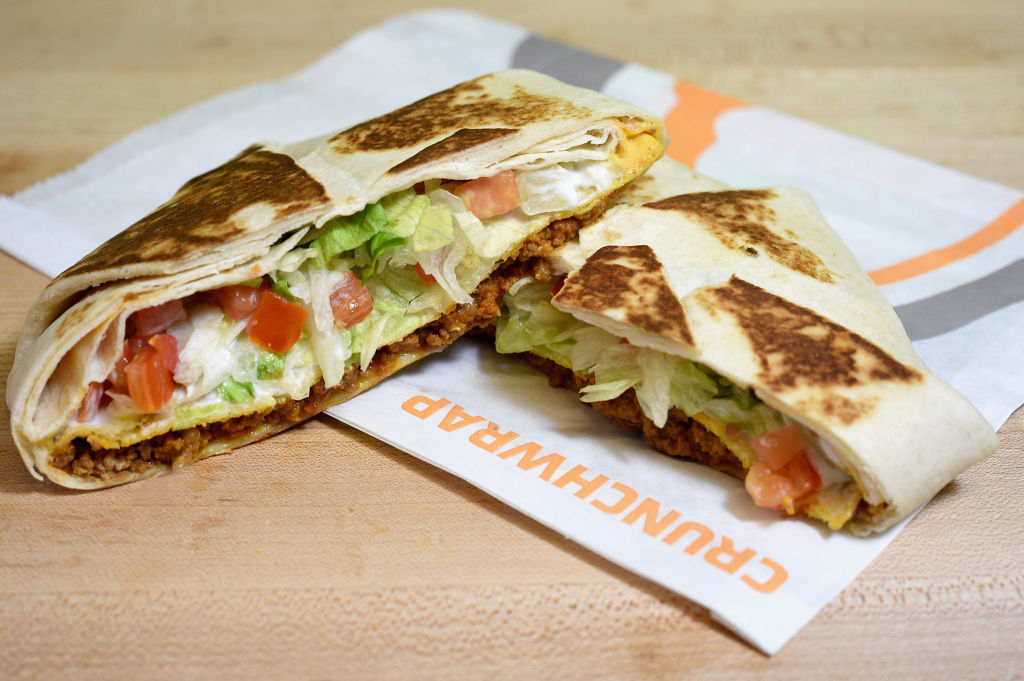 A cross-section of a Taco Bell Crunchwrap Supreme, showing layers of seasoned ground beef, lettuce, tomatoes, sour cream, and a crunchy tostada shell inside a folded tortilla
