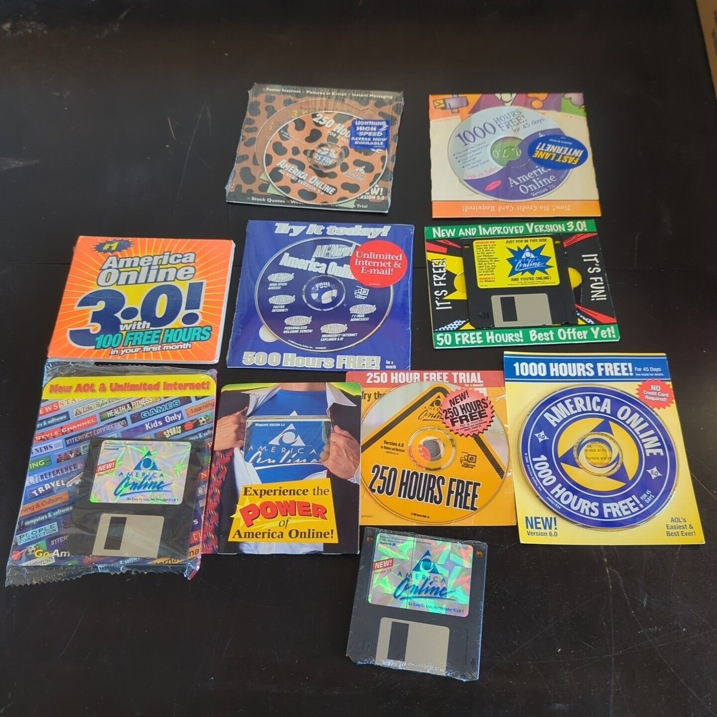Various old AOL CDs and floppy disks are spread on a surface, advertising free hours of internet service ranging from 50 to 1000 hours