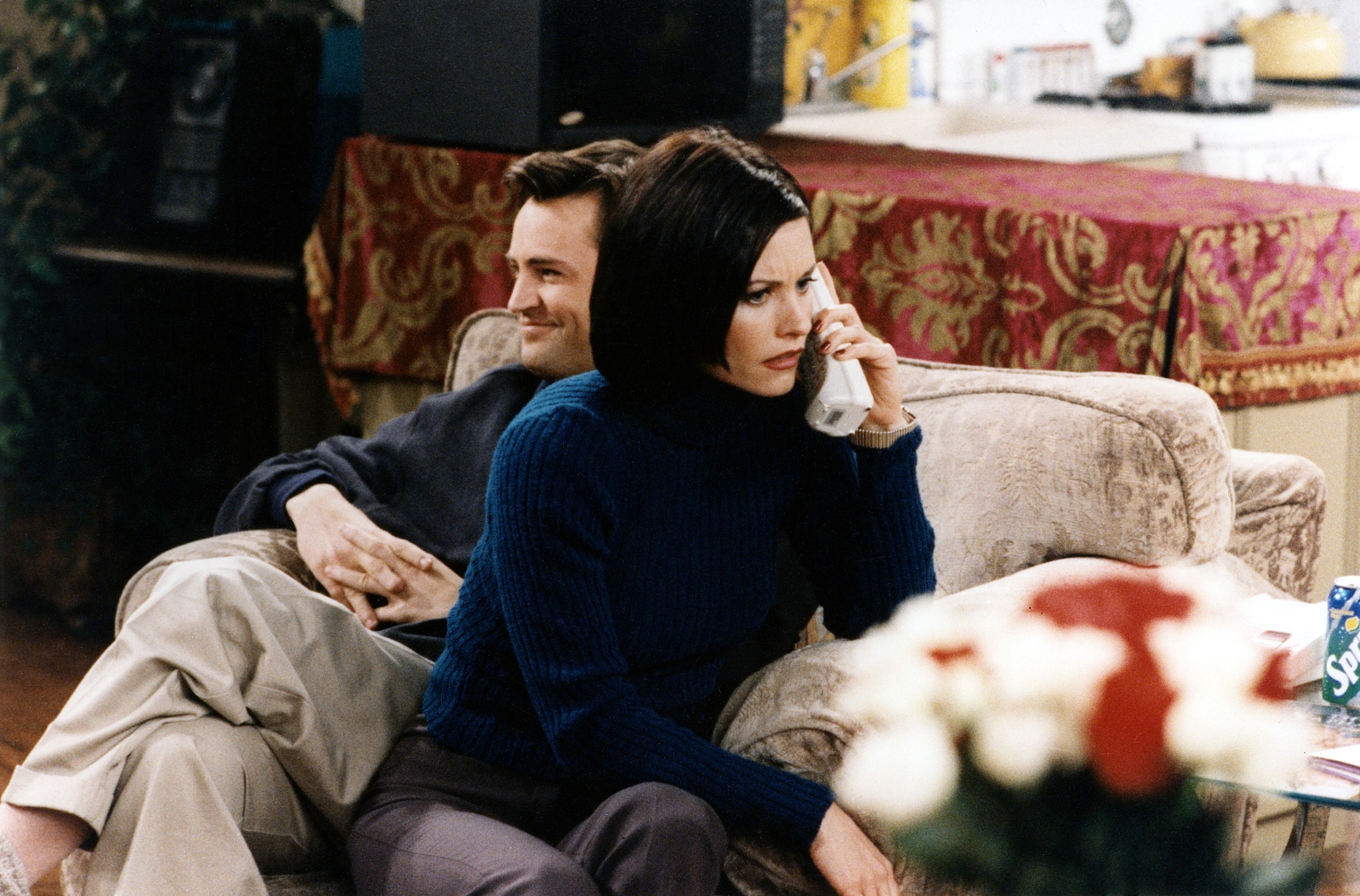 Courteney Cox and Matthew Perry in a living room scene, with Courteney Cox on the phone and Matthew Perry casually leaning back on the couch