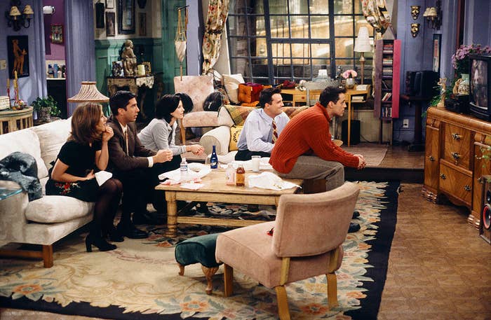 Jennifer Aniston, Courteney Cox, Lisa Kudrow, Matt LeBlanc, Matthew Perry, and David Schwimmer sit around a coffee table watching television in a living room set