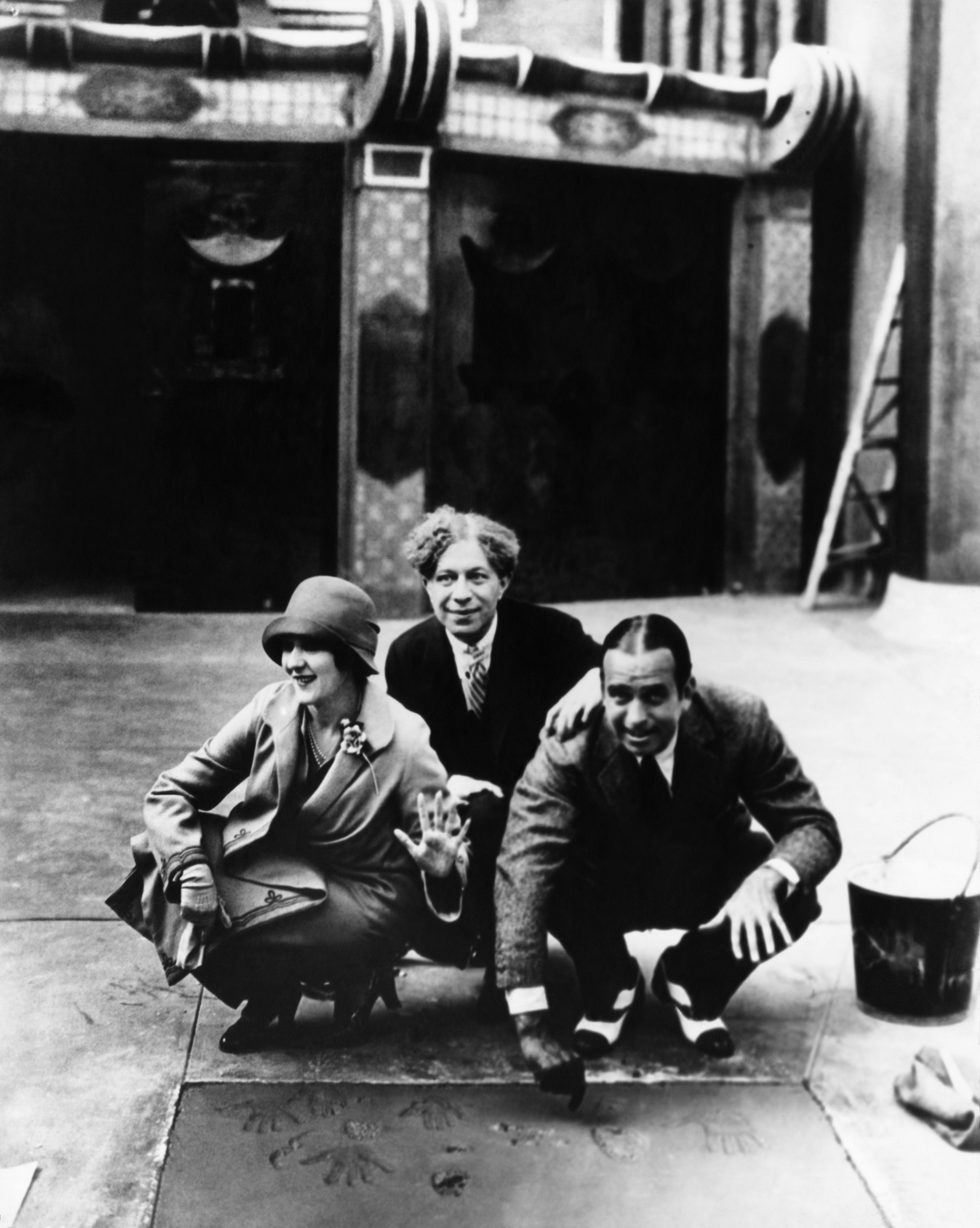 Clara Bow, Sid Grauman, and Harold Lloyd are seen posing with their handprints on the sidewalk during a commemorative event