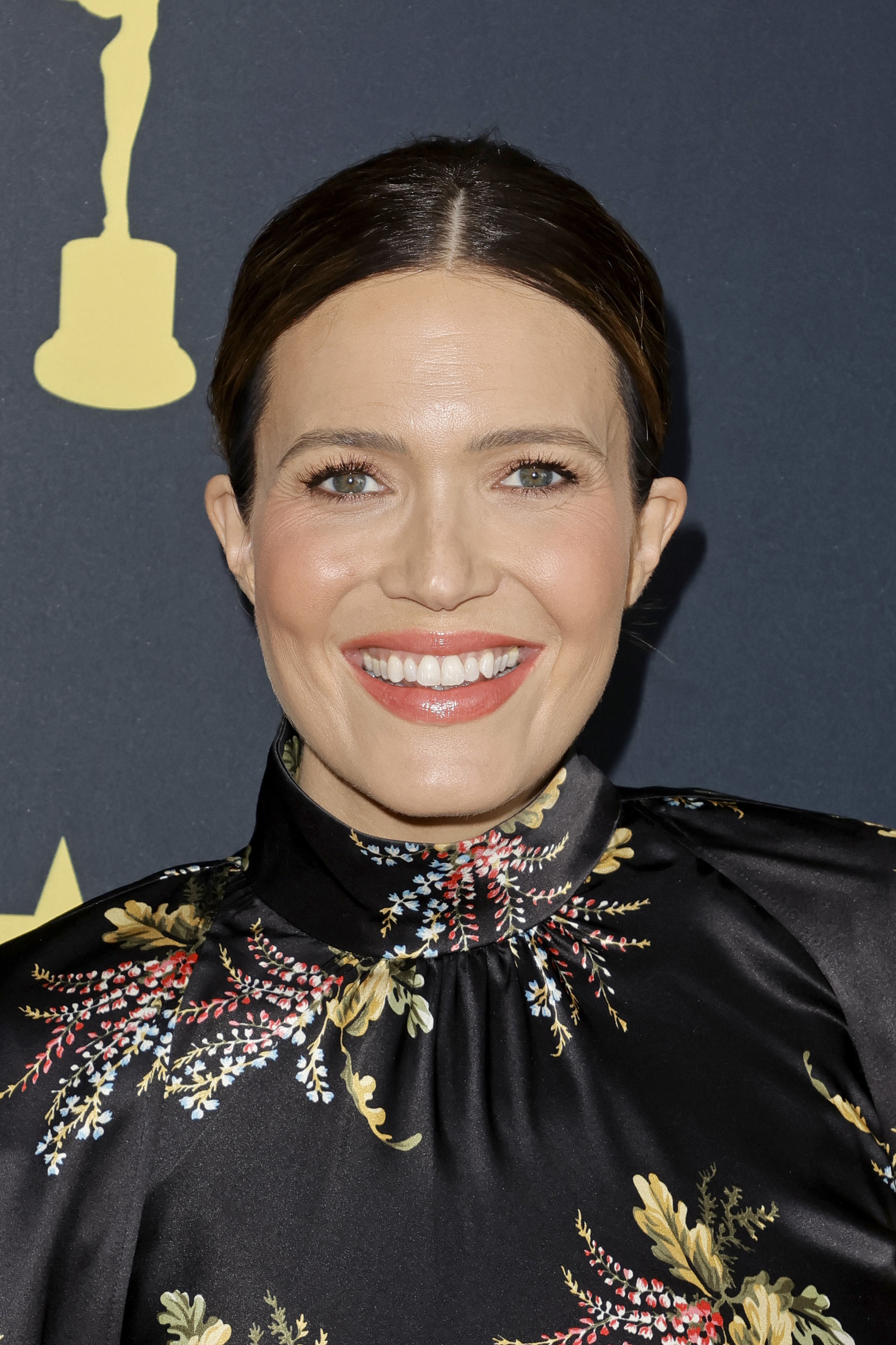 Mandy Moore smiling at a formal event, wearing a high-neck floral dress