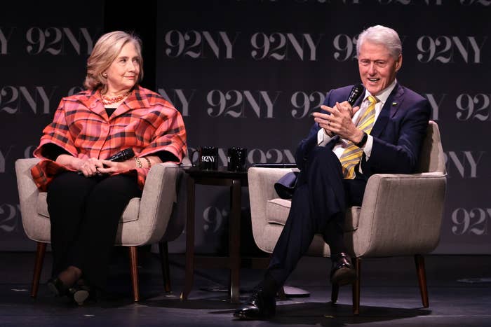 Hillary Clinton and Bill Clinton sit in chairs on stage at 92NY event; Hillary wears a patterned blazer, Bill wears a suit and tie, speaking into a microphone