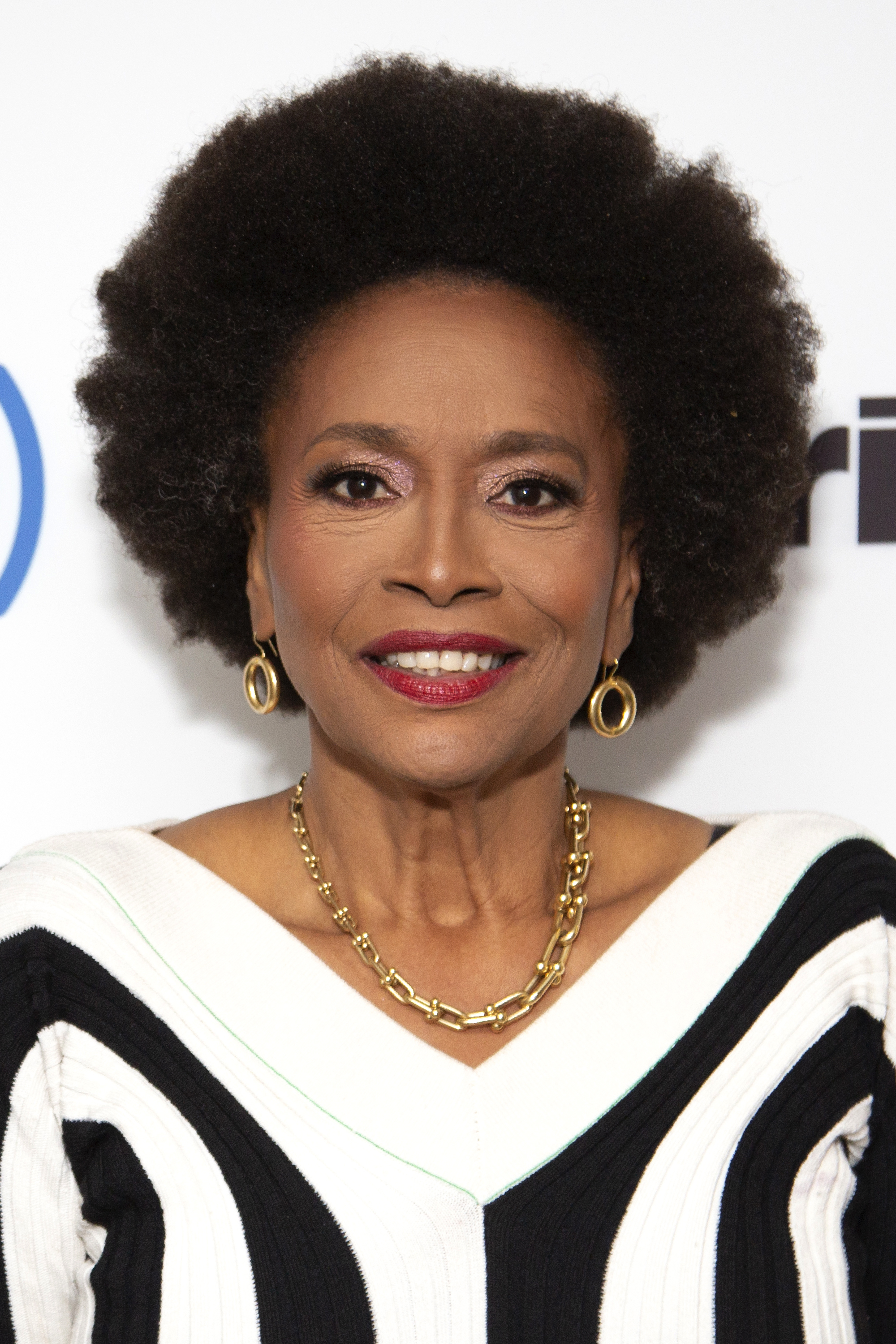 Jenifer Lewis at a public event wearing a stylish black-and-white outfit with gold hoop earrings and a gold necklace