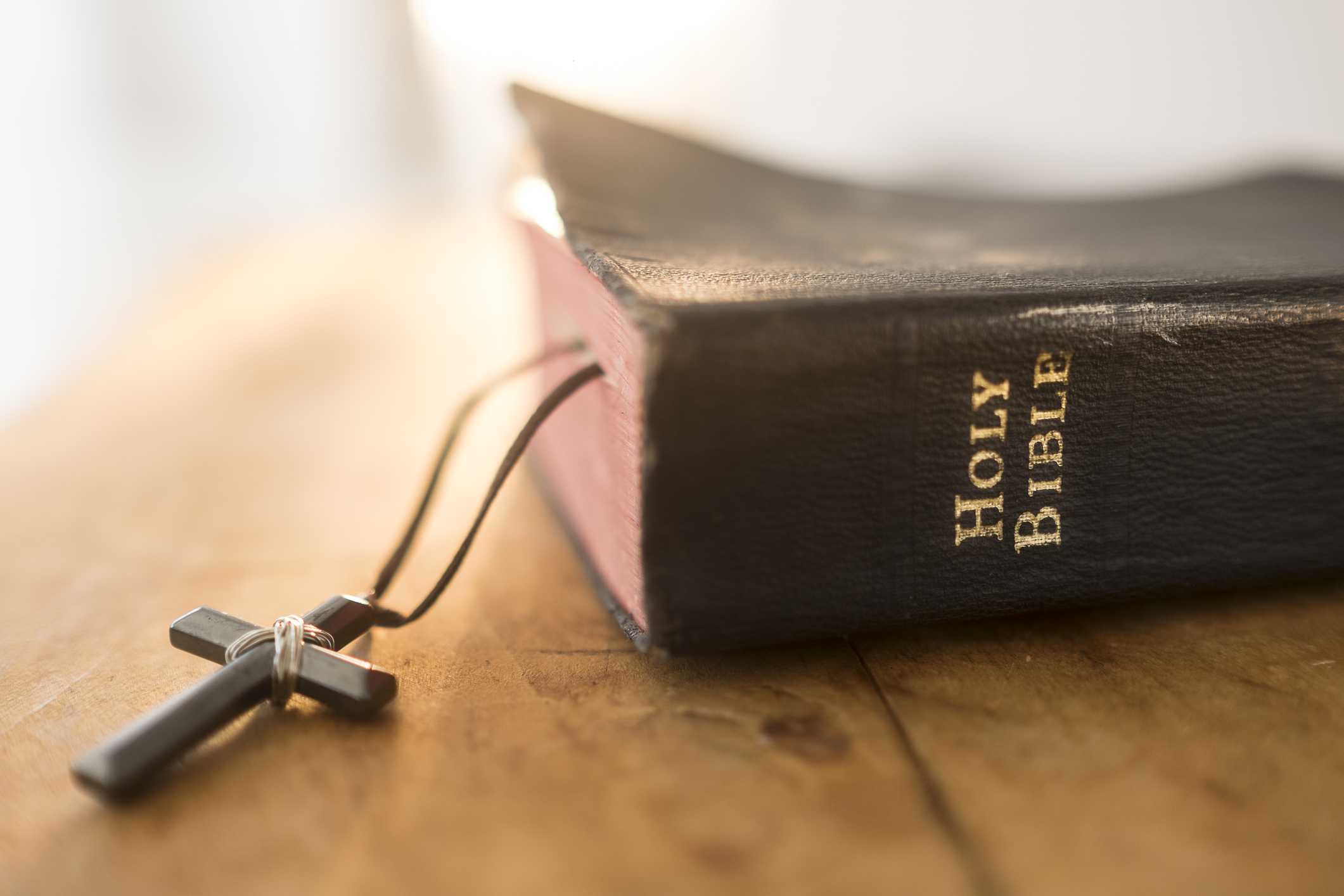 A Holy Bible resting on a wooden surface with a black cross necklace draped over it