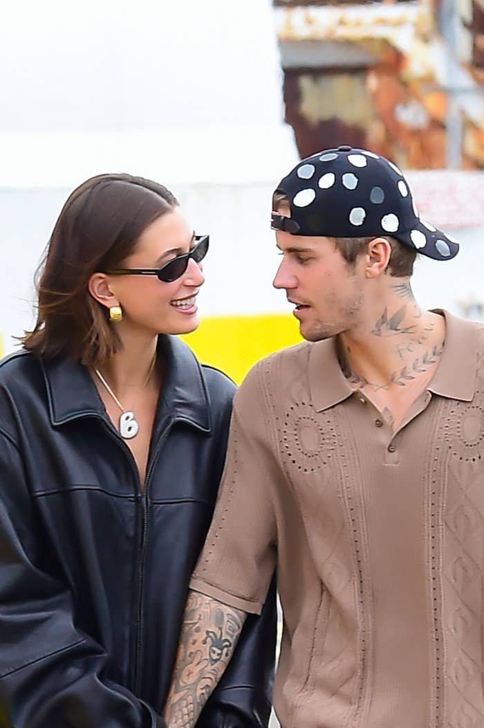 Hailey Bieber and Justin Bieber walk closely together, Hailey in a leather jacket and sunglasses, Justin in a knit shirt and cap