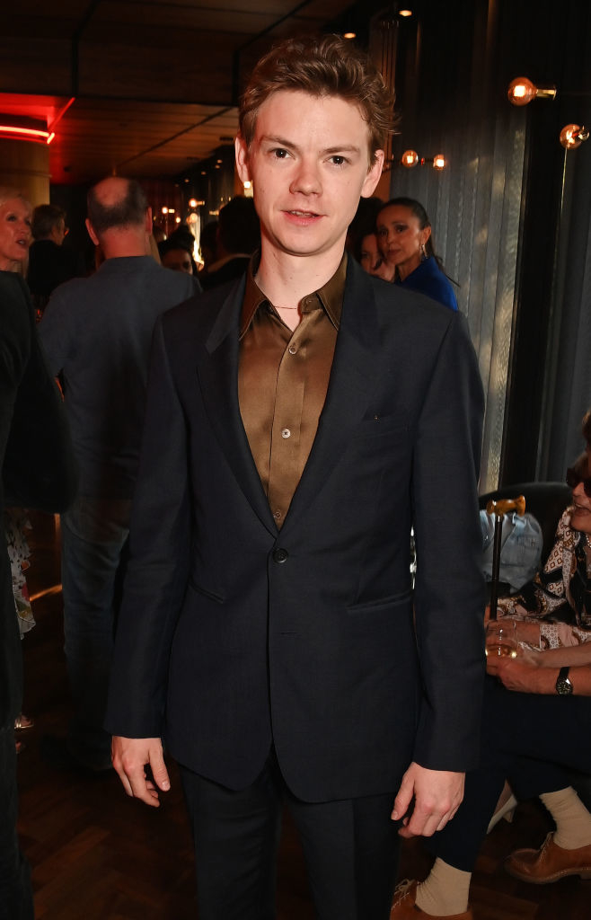 Thomas Brodie-Sangster at an indoor event, dressed in a dark suit with a bronze shirt