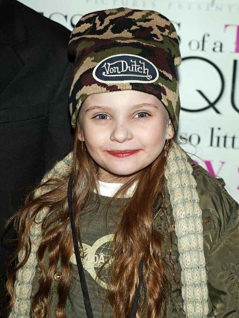 A young Abigail Breslin wearing a camouflage beanie and a scarf, smiling at an event