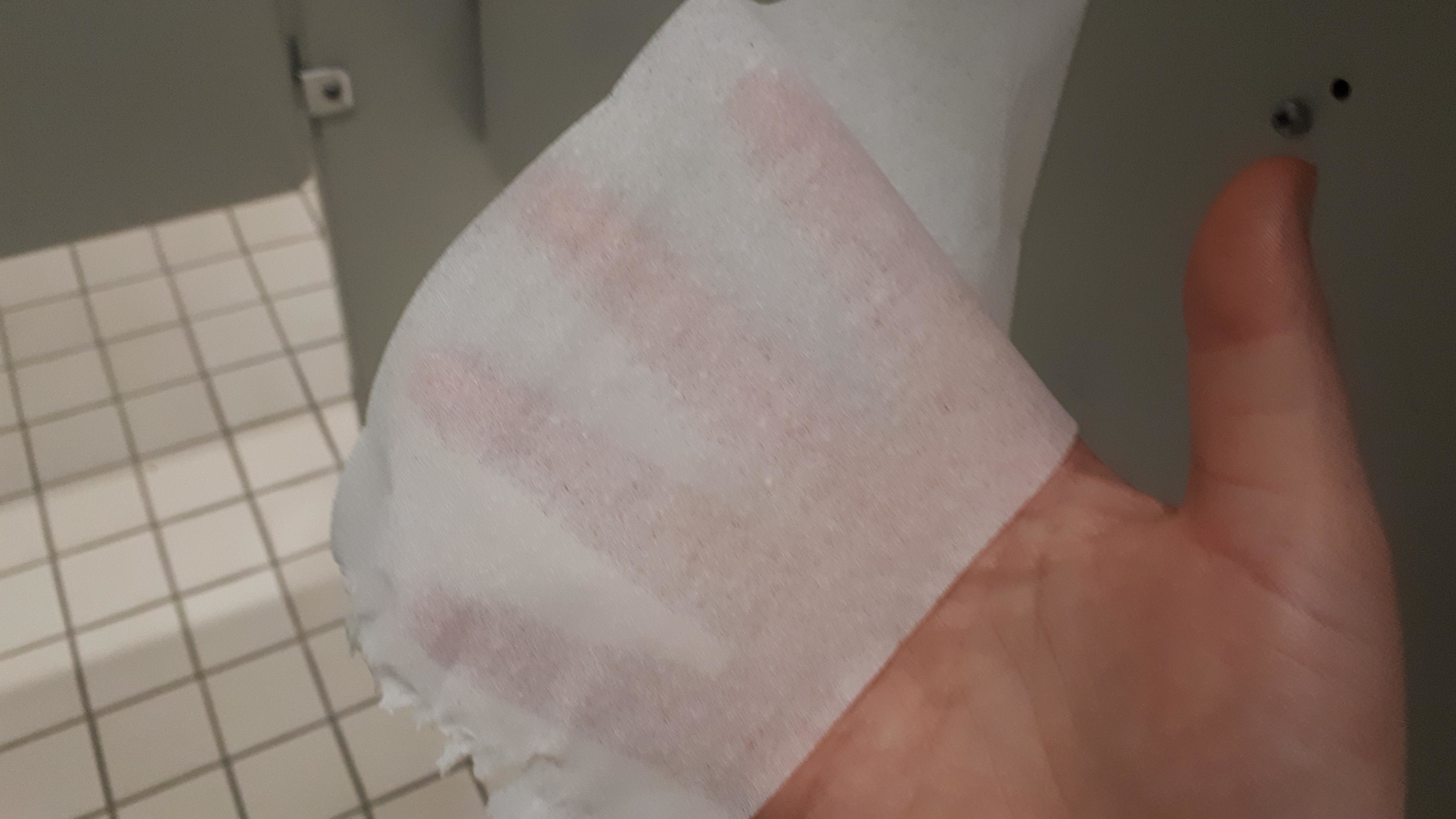 A person holding a semi-transparent hygienic wipe in a tiled restroom area