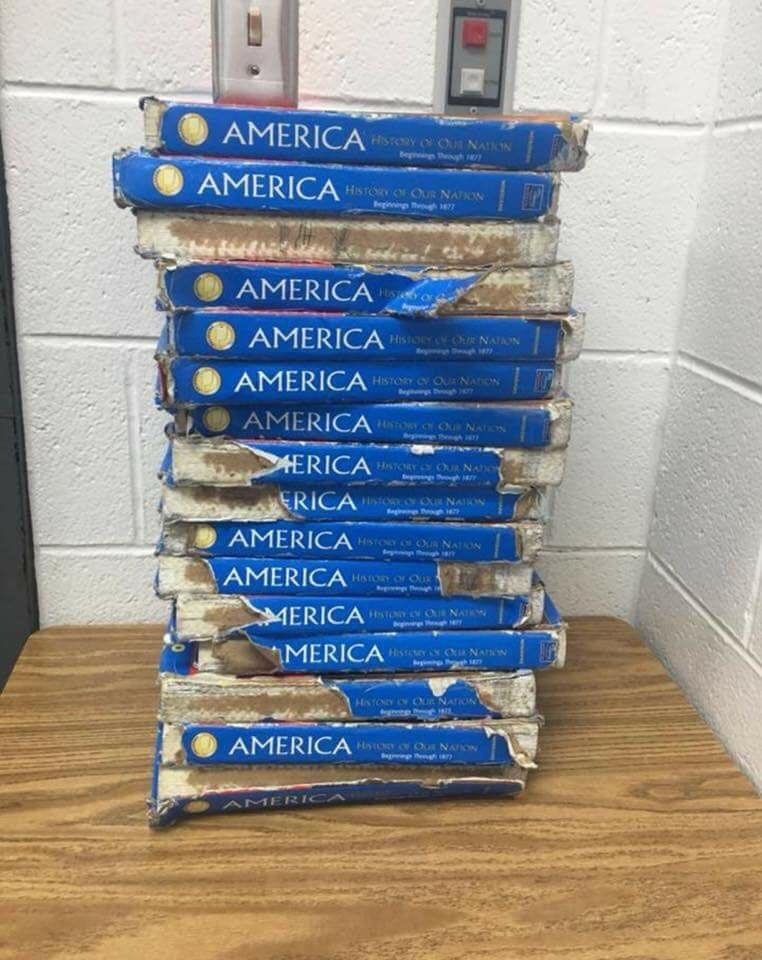 A stack of worn and damaged history textbooks titled &quot;America: History of Our Nation&quot; is piled on a table