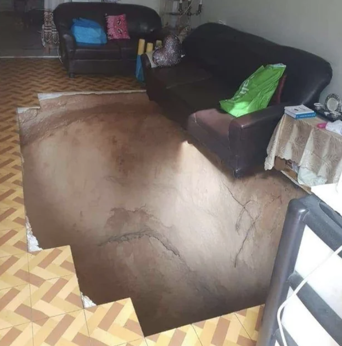 A large sinkhole has formed inside a living room, taking up most of the floor space between two brown couches