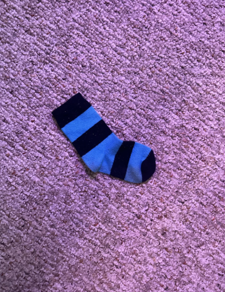 A blue and dark blue striped sock lays on a textured carpet