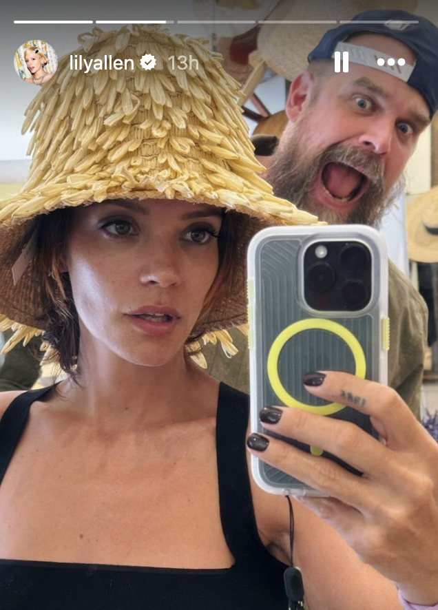 Lily Allen takes a selfie in a wide-brimmed textured hat. A David Harbour poses enthusiastically poses in the background