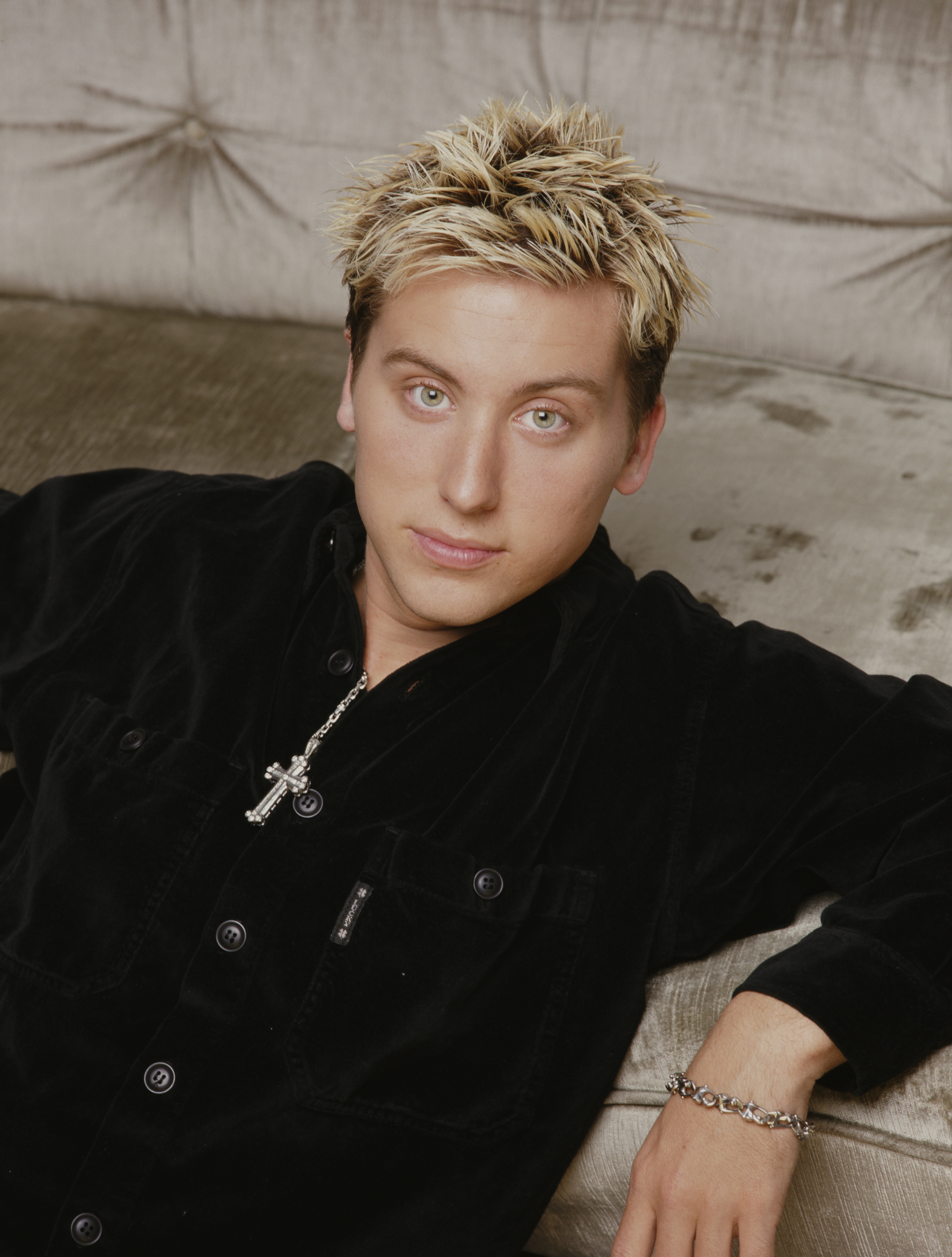 Lance Bass showing his spiked blonde-tipped hairstyle while lounging in a button-up top and silver jewelry