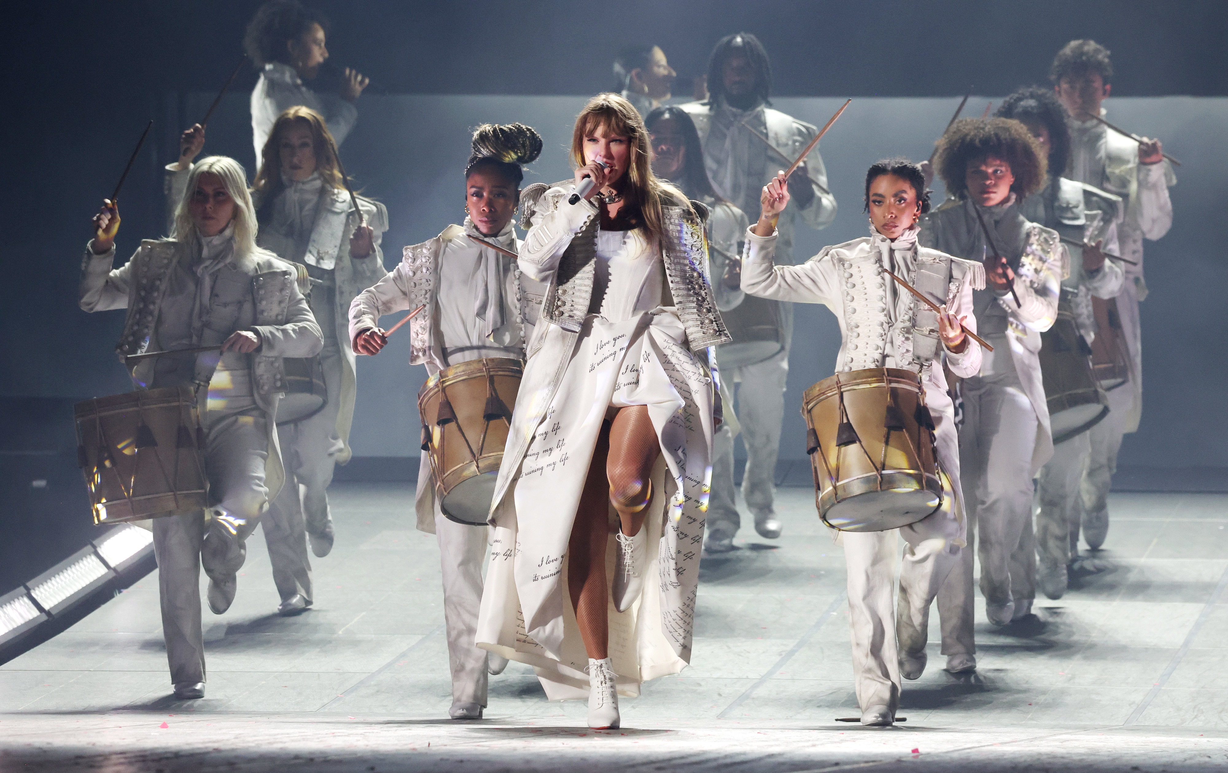 Taylor Swift performs on stage leading a group of drummers in similar attire during a concert