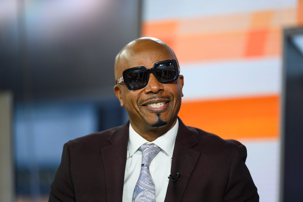 MC Hammer wearing a suit, tie, and sunglasses, smiling during an interview