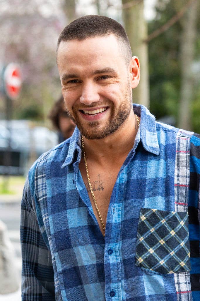 Man smiling, wearing a blue plaid shirt with contrasting patterns, and a gold chain necklace