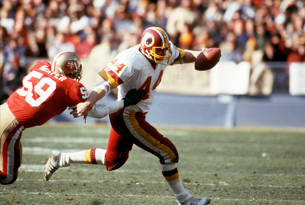 A Washington player, John Riggins, stiff-arms a San Francisco defender, Willie Harper, while running with the ball.