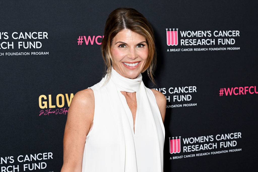 Lori Loughlin poses in elegant sleeveless white attire at the Women&#x27;s Cancer Research Fund event. Background features event logos and #WCRFCure hashtags